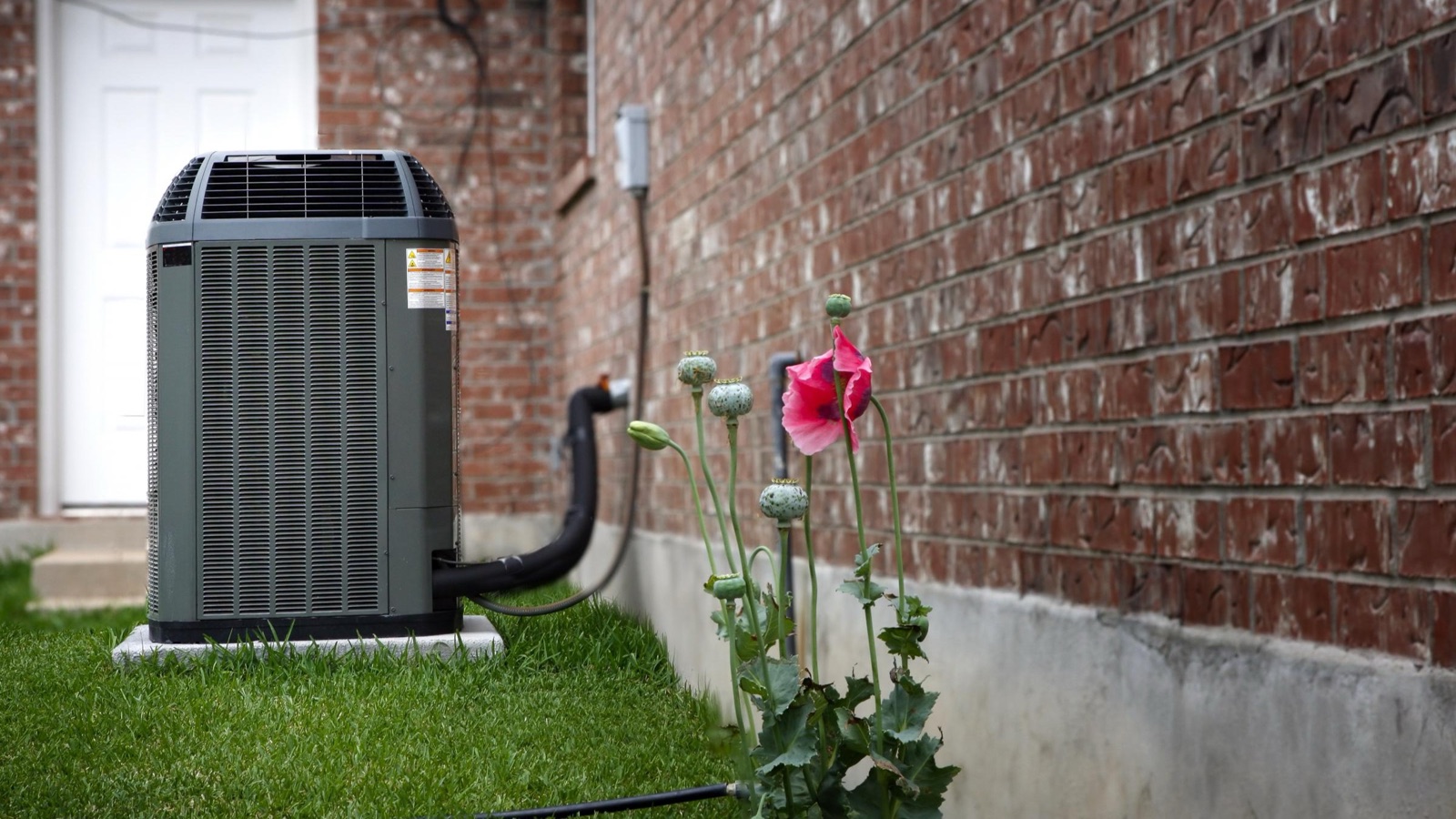 Residential air conditioning condenser beside a brick home